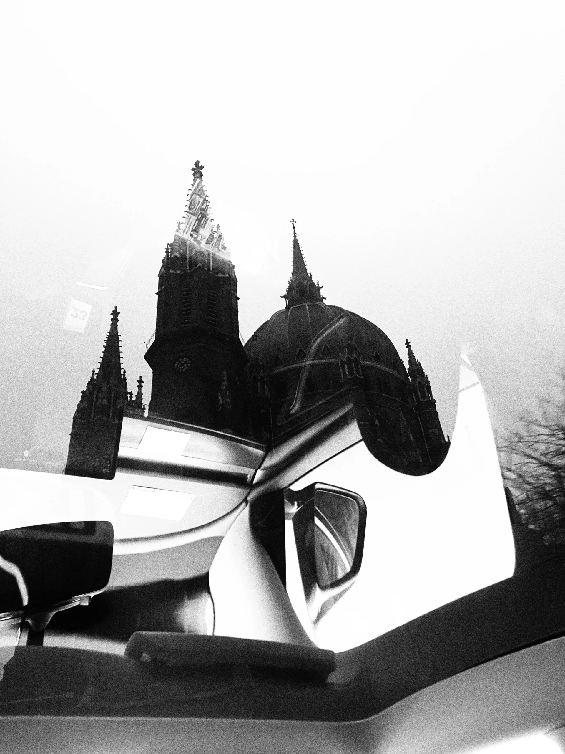 Black and white frame: Gothic spires and the roof of a car