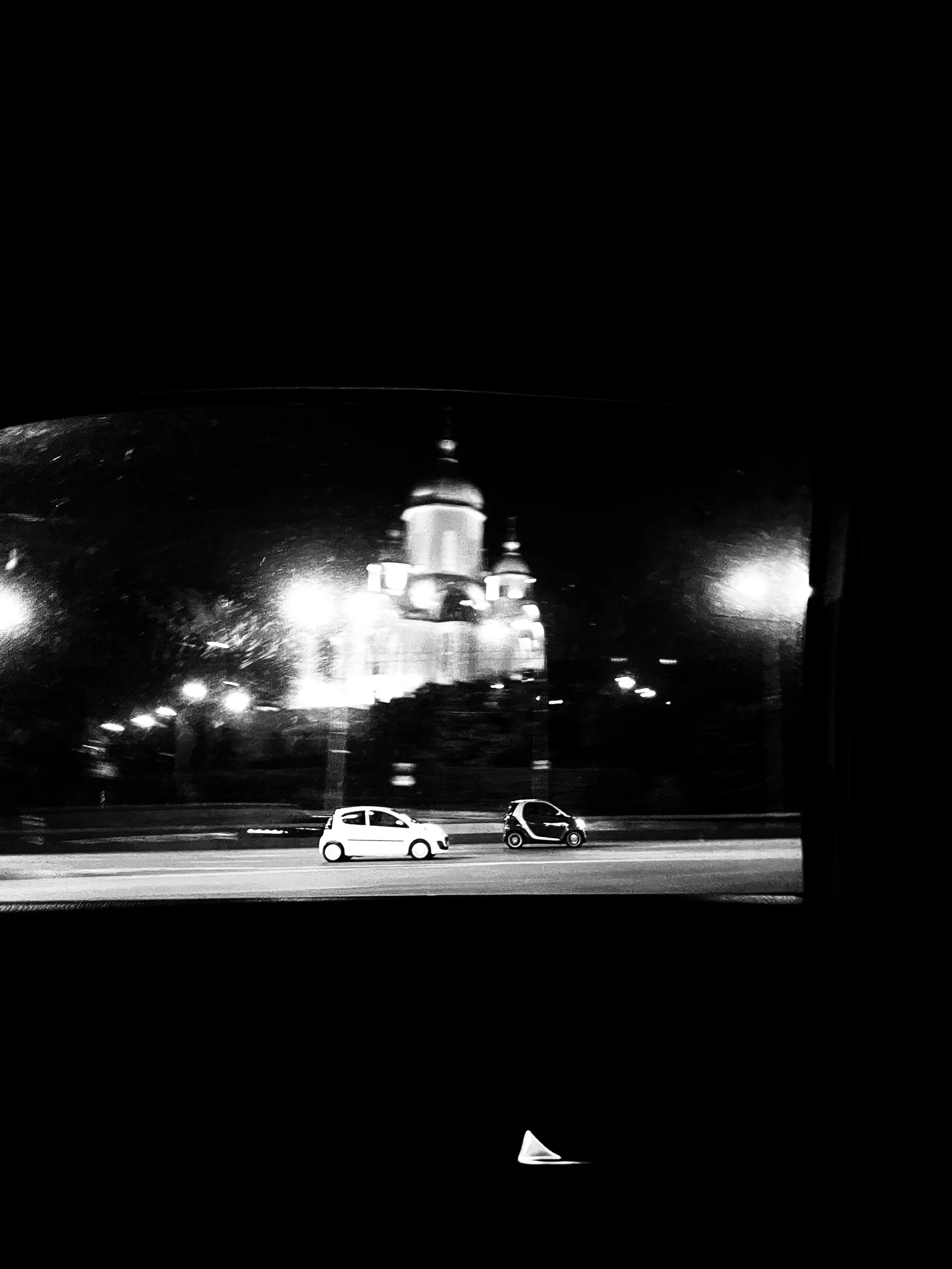 Black and white night shot through a car window: a lit church with domes and two cars