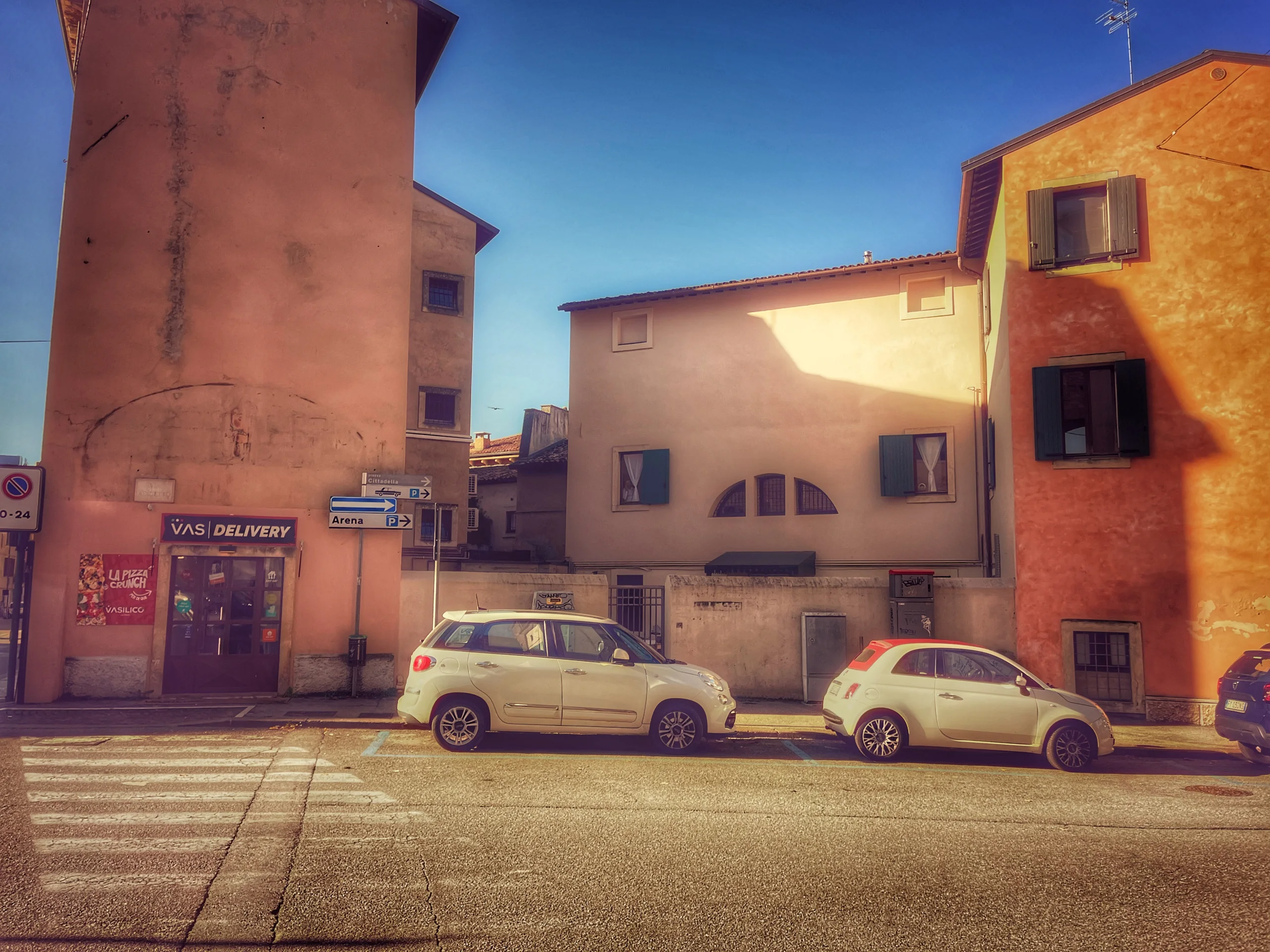 Street with orange houses and small cars under a blue sky