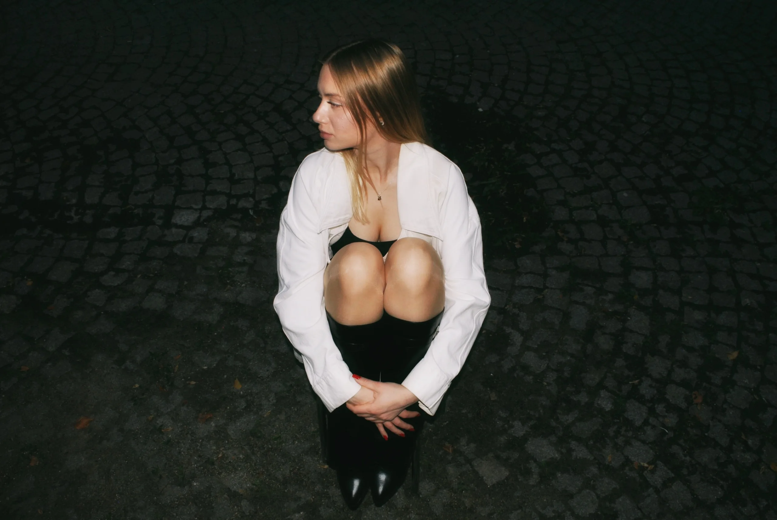 Night flash photo: a woman in a white shirt crouching on cobblestones