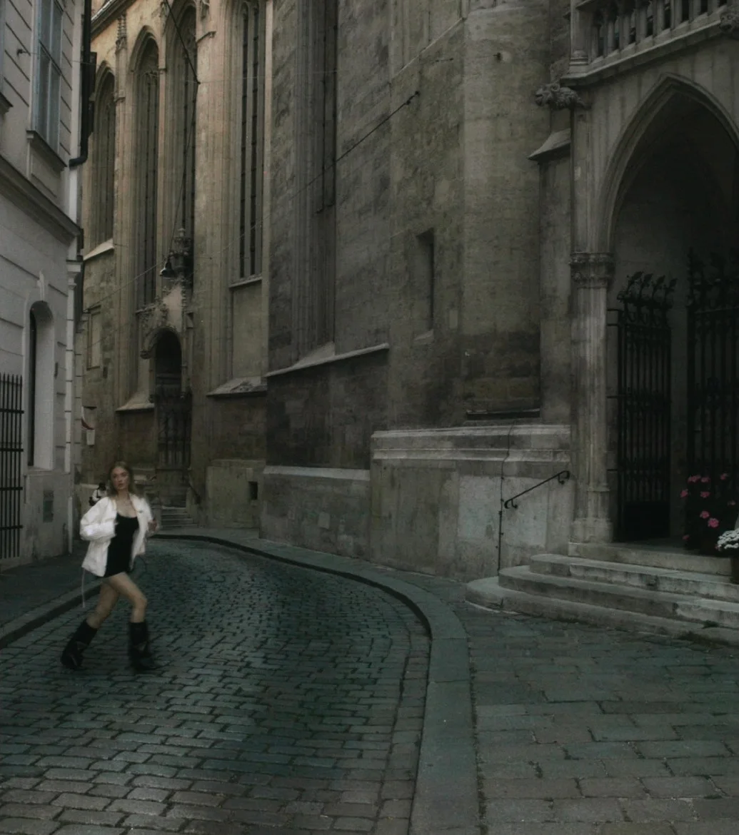 Narrow cobbled street with a Gothic facade, a woman in white in the distance