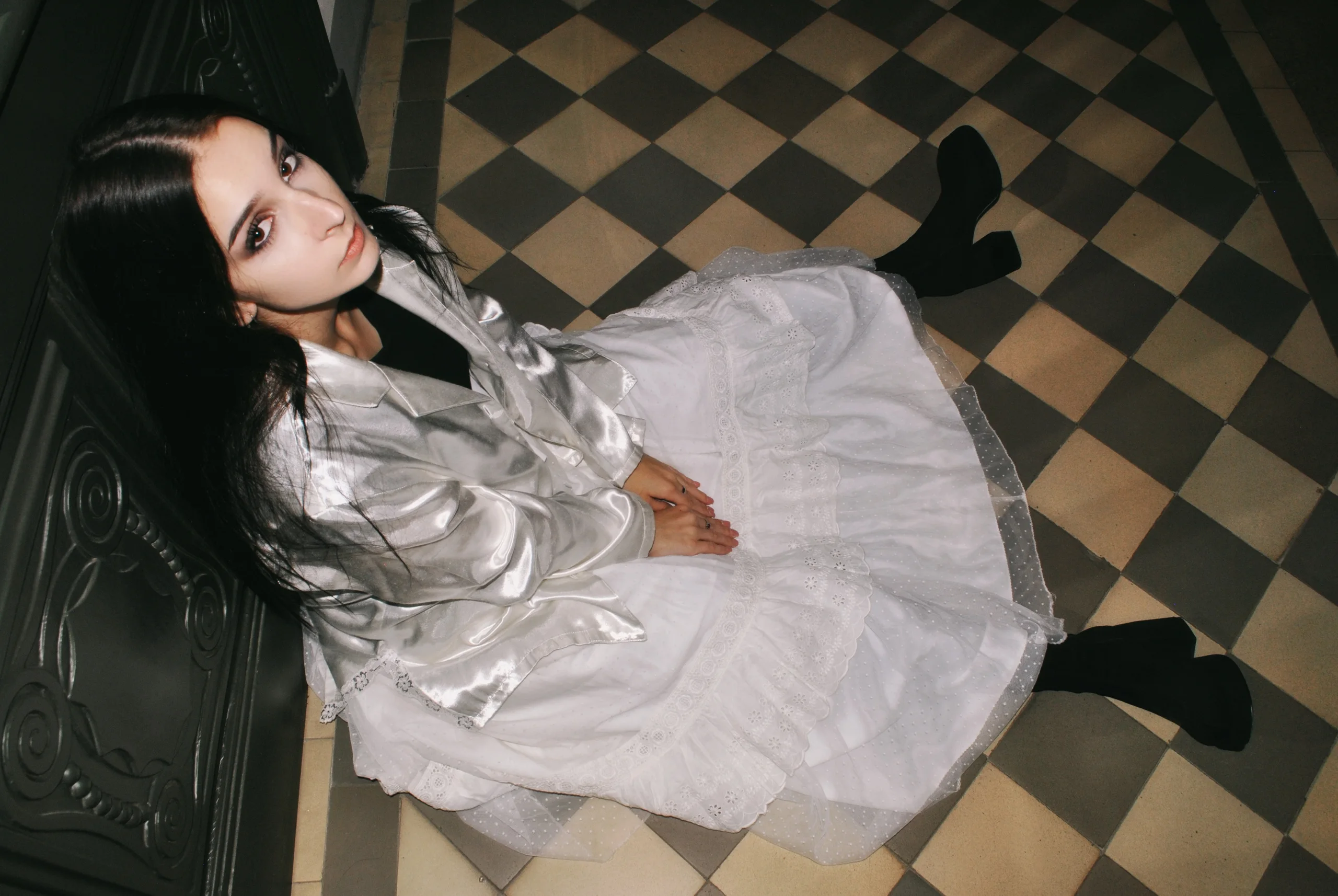 Model in a white satin shirt and lace skirt on a checkered floor, shot from above
