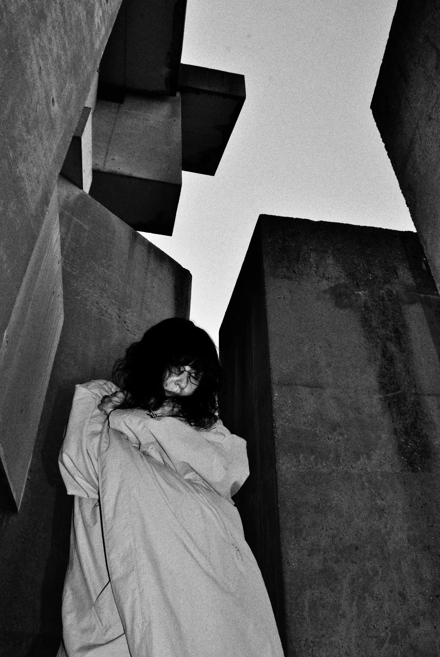 Model in a light coat among the concrete blocks of the Wotruba Church, grainy black and white